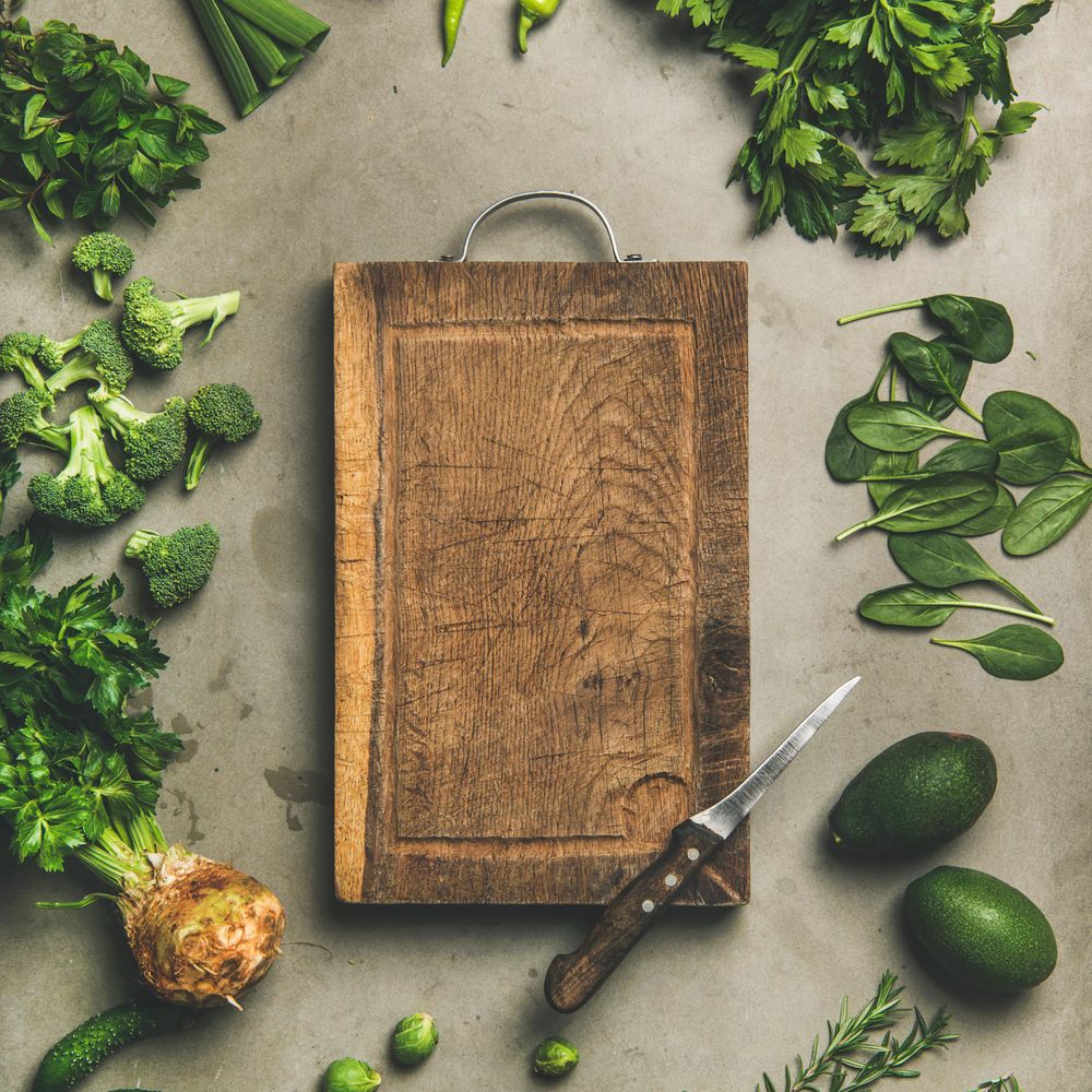 Arrangement of fresh green garden vegetables on concrete surface, with wooden board, square crop