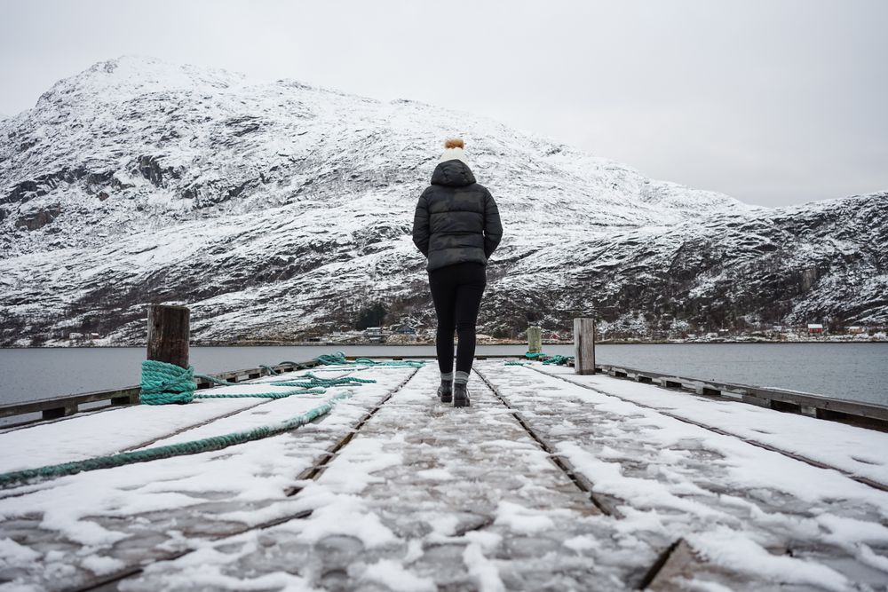 Woman on waterfront against small town at snowy foothill