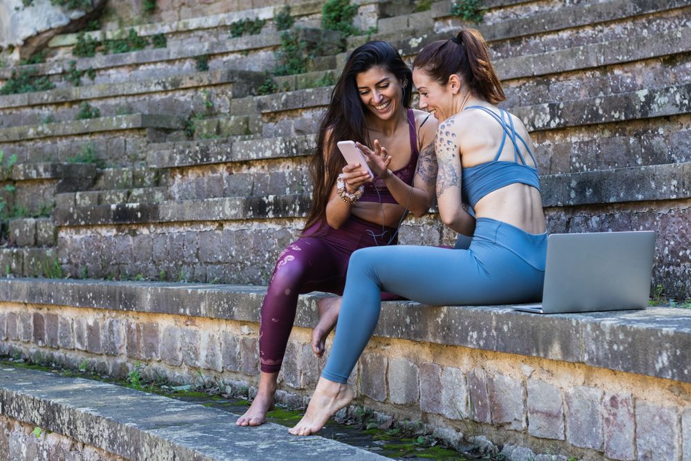 Smiling multiethnic women using smartphone after yoga practice