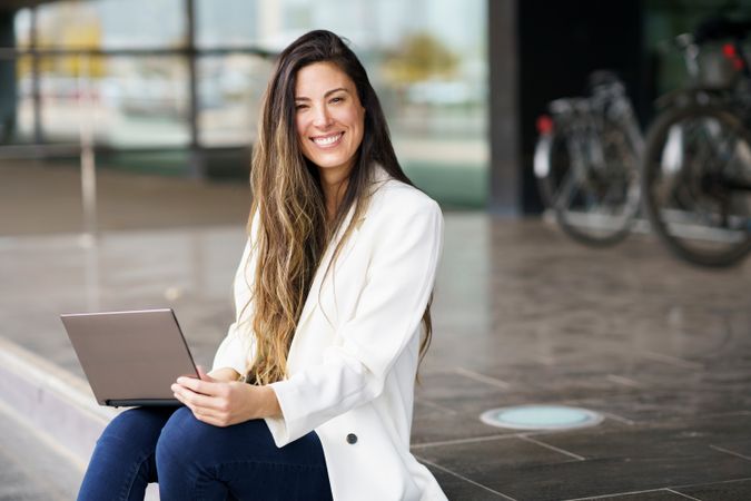 A Smiling Young Woman Happily Working on Her Laptop While Outdoors in a Bright Environment