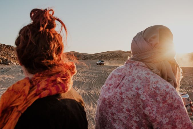 Anonymous travelers looking at car in desert
