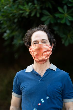 Man with red gingham PPE mask smiling and looking at camera