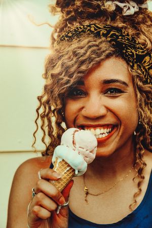 Vertical shot of smiling Black female smiling with an ice cream cone in the sun, close up