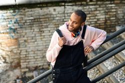 Smiling male in overalls and hoodie leaning on railing of stairs outside