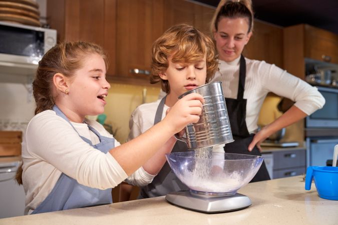 Cheerful girl sifting flour into bowl during cooking process