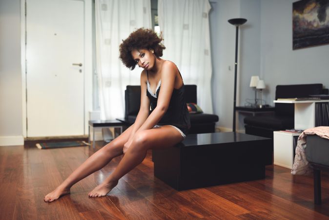Female with curly hair in underwear sitting casually on coffee table