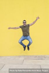 Joyful male standing outside jumping in front of yellow wall with open arms 0LmQR5