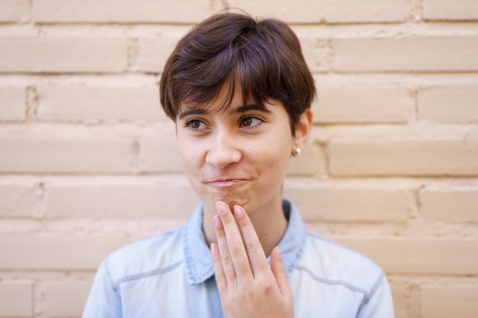A thoughtful young individual stands against a rustic brick wall, lost in deep contemplation