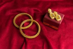 Beautiful shiny golden bangles and diamond studded traditional earrings on a red velvet background
