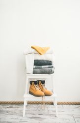 Pile of folded sweaters on light background with yellow boots, vertical composition, copy space