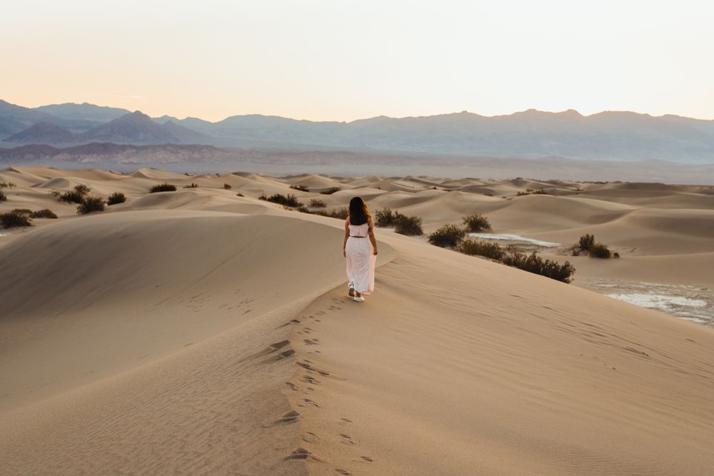 Back view of young woman walking in desert leaving footprints in dry sandy dunes in Death Valley