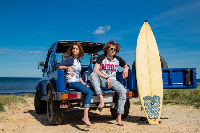 Couple with surfboard sitting on a car