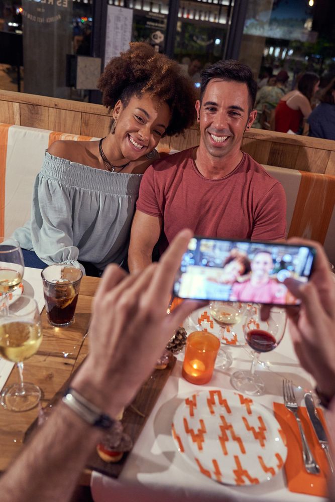 Crop man taking photo of multiethnic couple in bar
