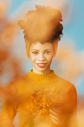 Studio shoot of Black woman holding orange flowers behind orange cloud effect