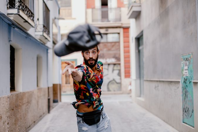 Young man throwing cap on alley