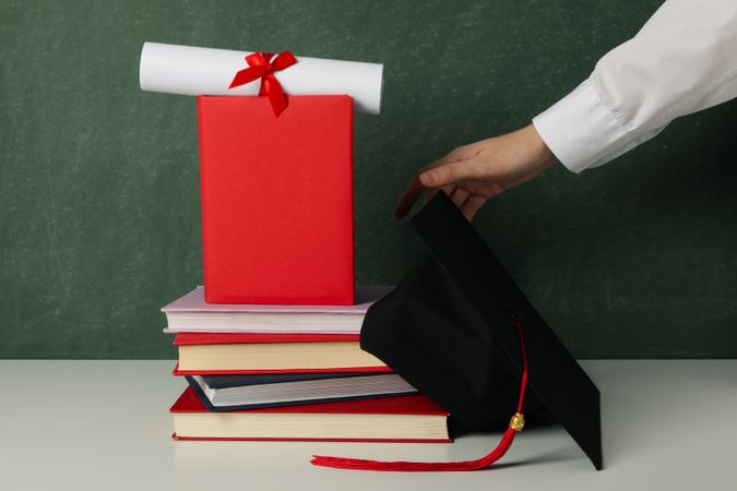 Graduation hat with books on a table on a dark background.