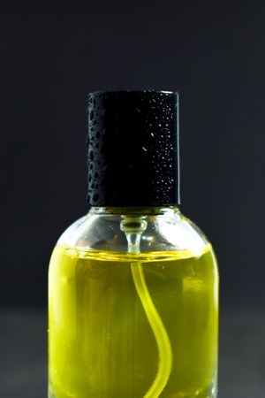 Close up of top of yellow bottle with droplets in dark studio