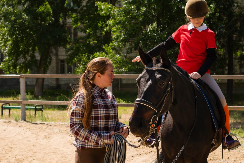 Instructor discusses technique with young rider during equestrian lesson.