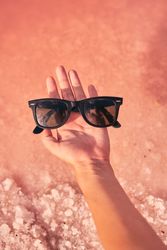 Female holding sunglasses above pink water