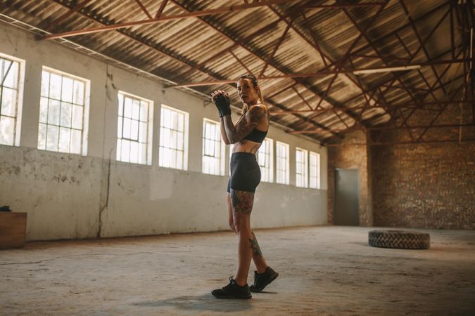 Full length of a woman in sportswear standing inside old factory shade