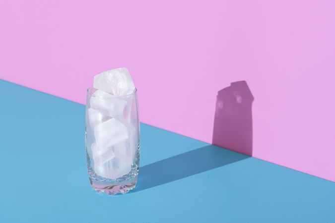 Ice cubes in a glass, in bright light, minimalist on a blue and pink background