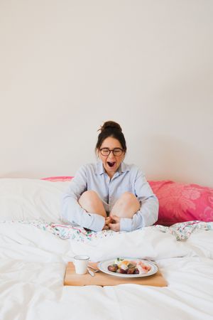 Young woman with breakfast on bed yawning