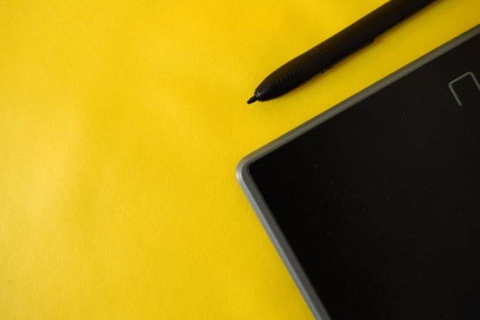 Stylus and corner of digital tablet on yellow table with space for text