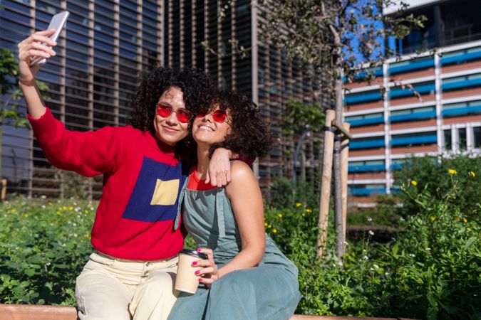 Female couple sitting on bench outside checking phone together