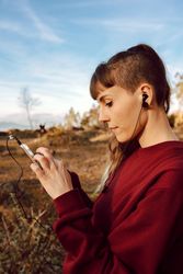 Young woman with piercing listening music on smartphone on hill