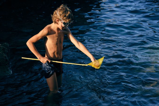 Shirtless boy with net in wavy ocean