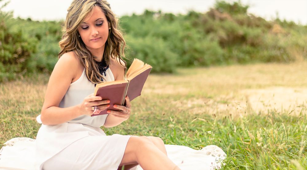Romantic woman reading a book sitting outdoors