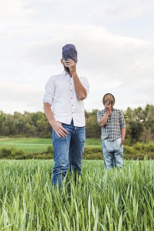 Two men in plaid shirt standing in oat field with forest in background