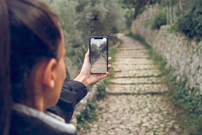 Crop of woman photographing stone path and nature on smartphone