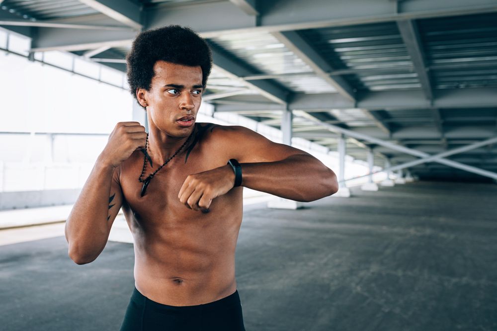 Athletic Black male doing boxing training under a bridge