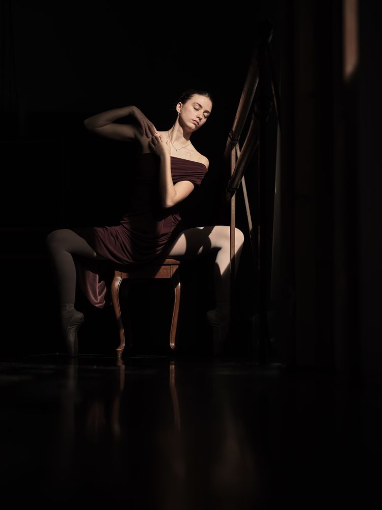 Ballerina sitting in plie on chair in dark room
