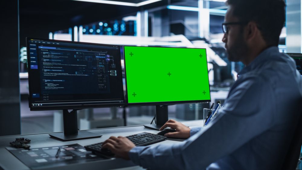 Professional Male IT Technical Support Specialist and Software Developer Working on Computer with Green Screen Mock-display in Monitoring Control Room. Programmer Fixing Hiccups in Service