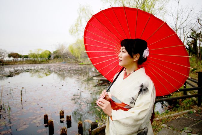 Woman in light kimono holding red umbrella standing on dock