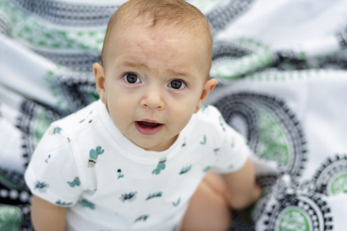 Joyful charming baby sitting on blanket and looking at camera