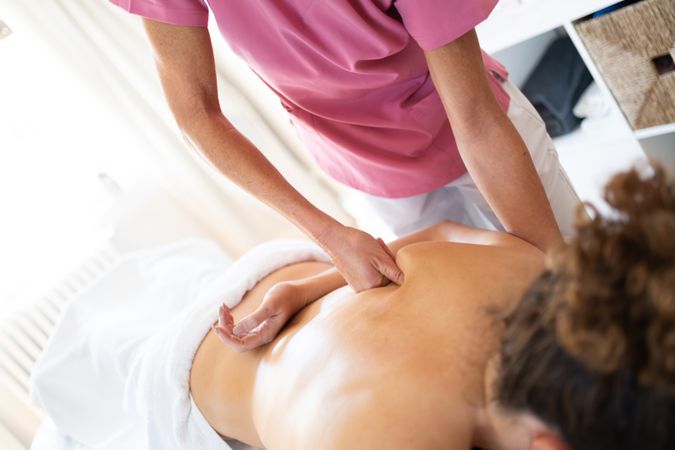 Masseuse massaging back of woman in spa salon using fists