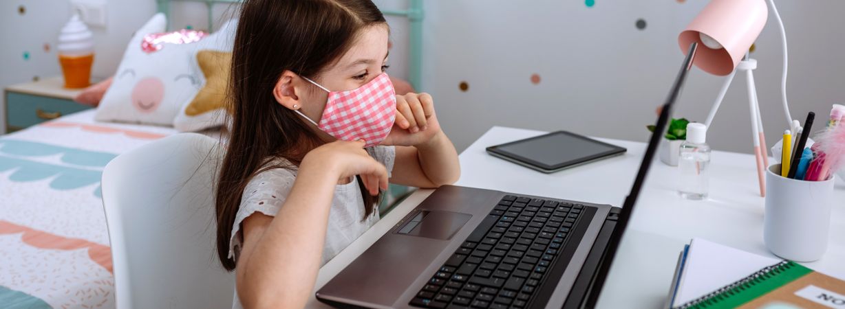 Little girl with mask using laptop