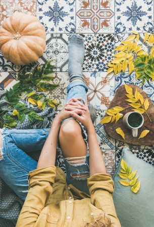 Woman sitting on colorfully tiled balcony with fall leaves, squash, and mug