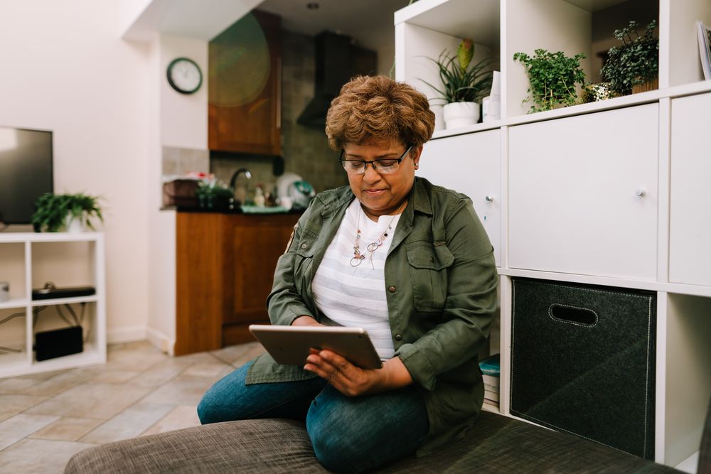 Smiling older Black woman sitting on sofa reading from tablet