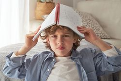 Grumpy boy covering head with copybook