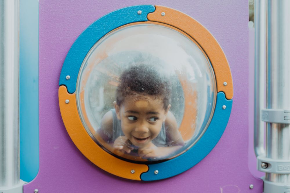 Funny Black boy behind porthole on playground