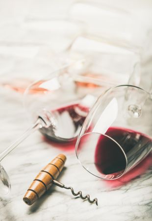 Glasses of red wine laying on marble background with corkscrew