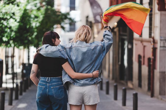 Lesbian couple with LGBT flag walking on street