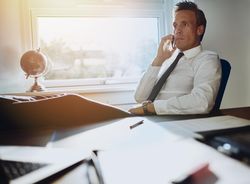 Man in shirt and tie taking phone call while resting legs on desk