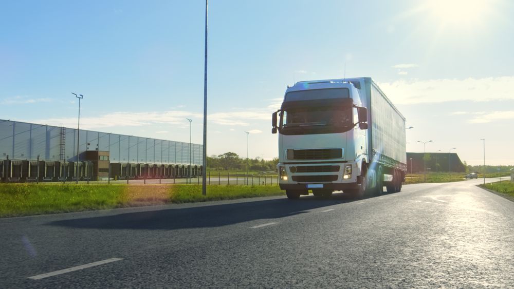 Semi Truck with Cargo Trailer Moves on the Industrial Area Empty Road With Sun Shining in the Background.