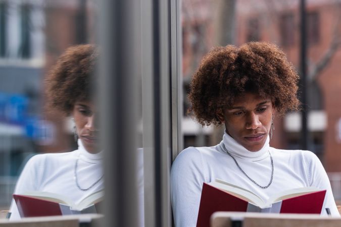 Relaxed young Black man reading book in street cafe