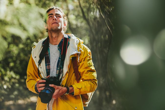 Portrait of a man wearing jacket and backpack walking in a forest holding a dslr camera